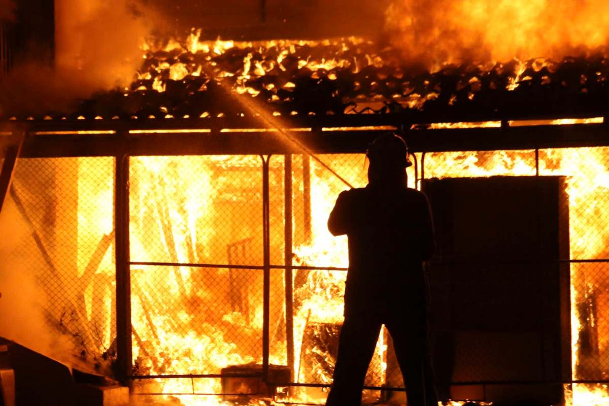 A firefighter uses a hose to extinguish a building engulfed in flames.