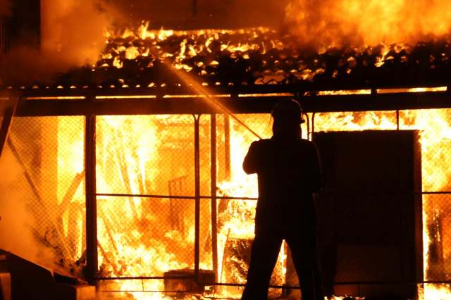 A firefighter uses a hose to extinguish a building engulfed in flames.
