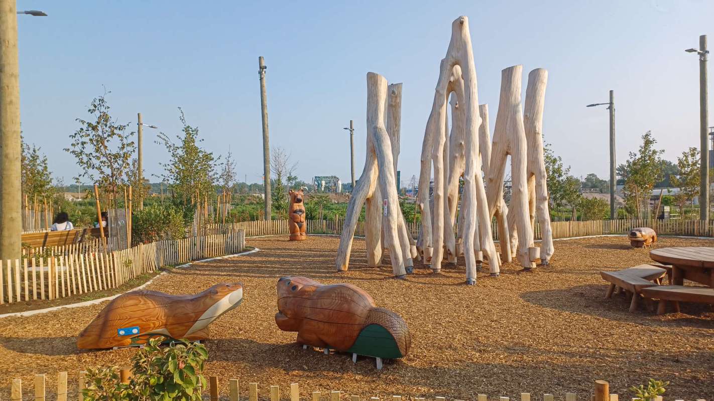 A playground featuring wooden animal sculptures and tall wooden poles surrounded by greenery.