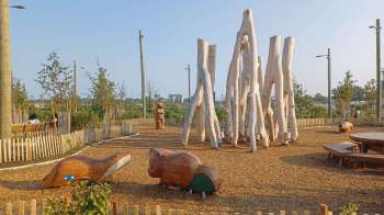 A playground featuring wooden animal sculptures and tall wooden poles surrounded by greenery.