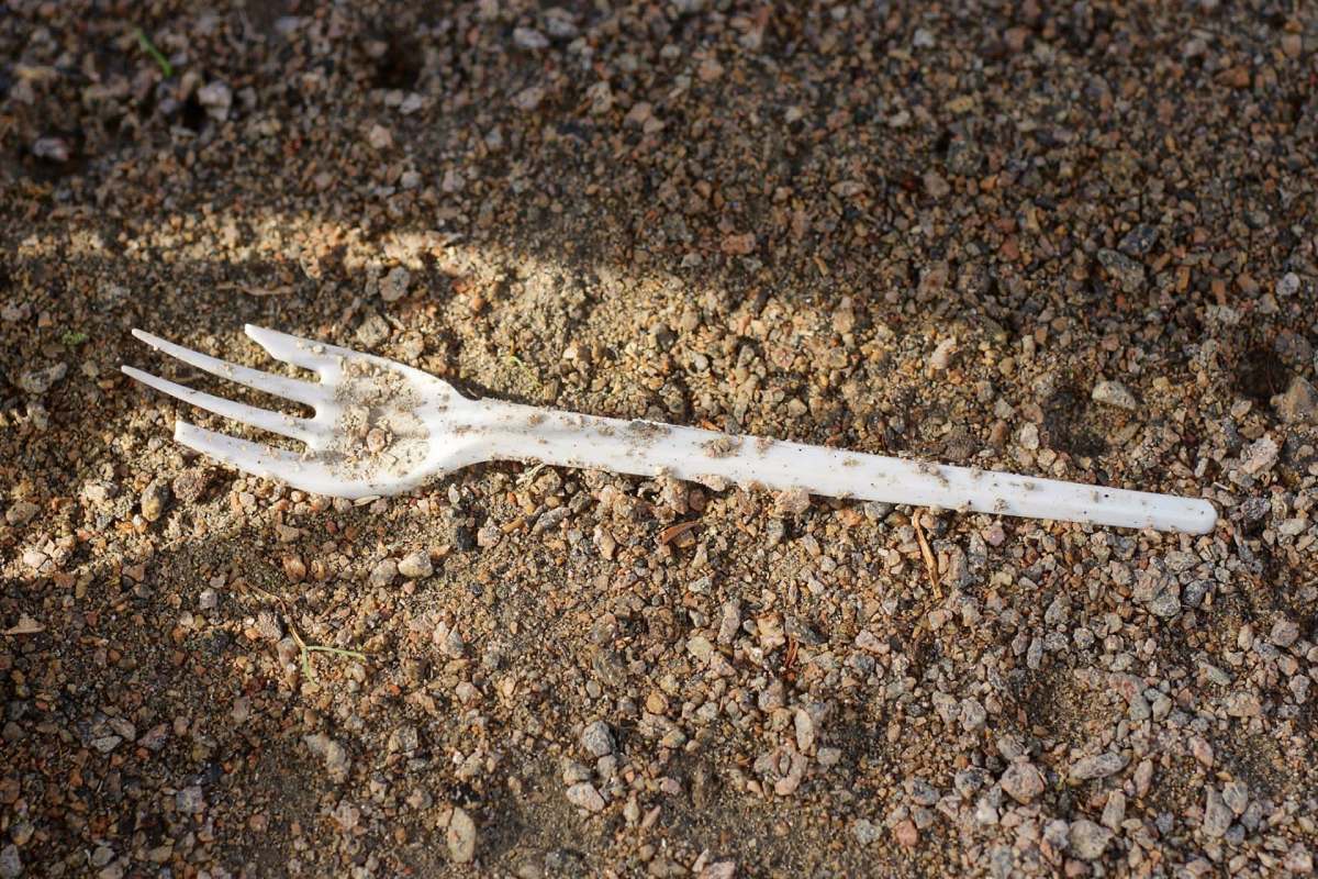 A plastic fork resting on a surface of dirt and small rocks.