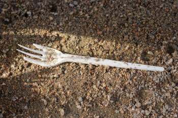 A plastic fork resting on a surface of dirt and small rocks.