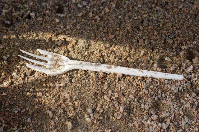 A plastic fork resting on a surface of dirt and small rocks.
