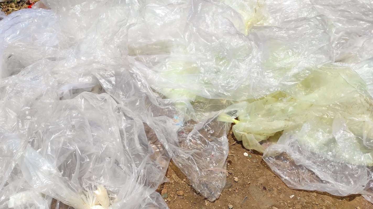 Discarded plastic bags and debris spread across a dirt surface.