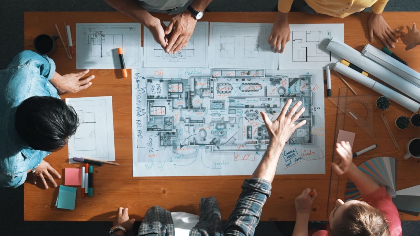 A group of people collaborates on architectural plans and diagrams on a wooden table.