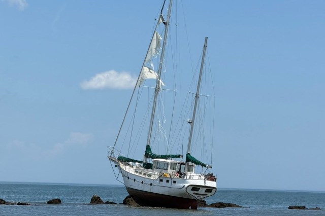 A sailboat is stranded on rocks near the shore under a blue sky.