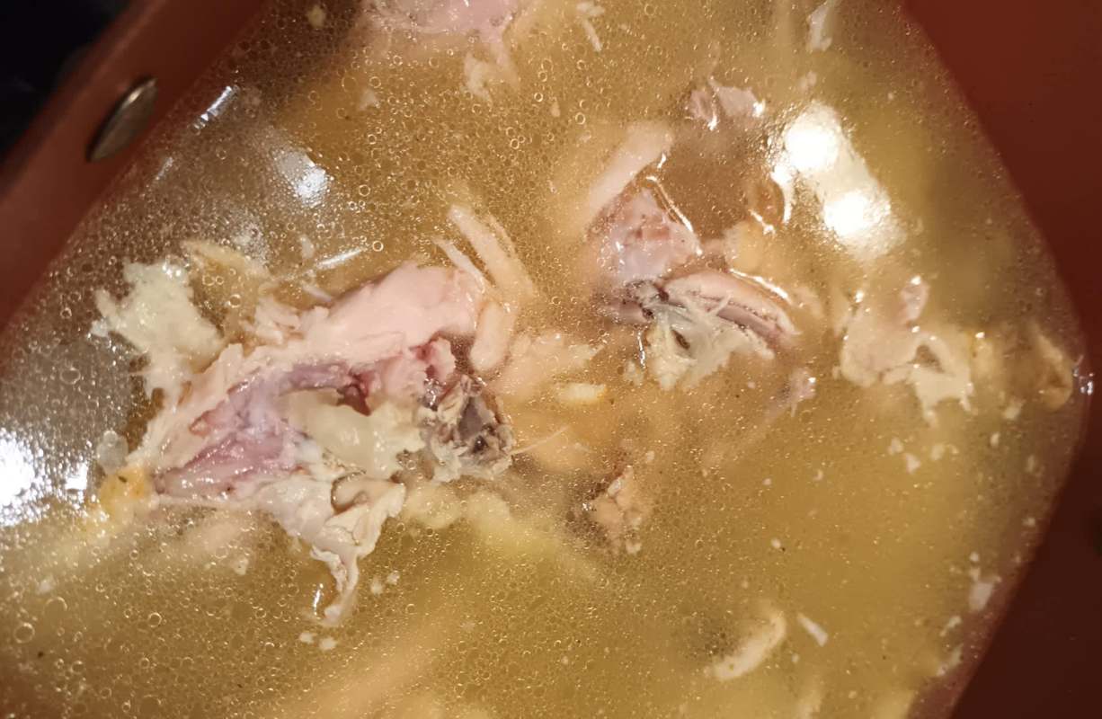 A pot filled with broth and pieces of cooked chicken.