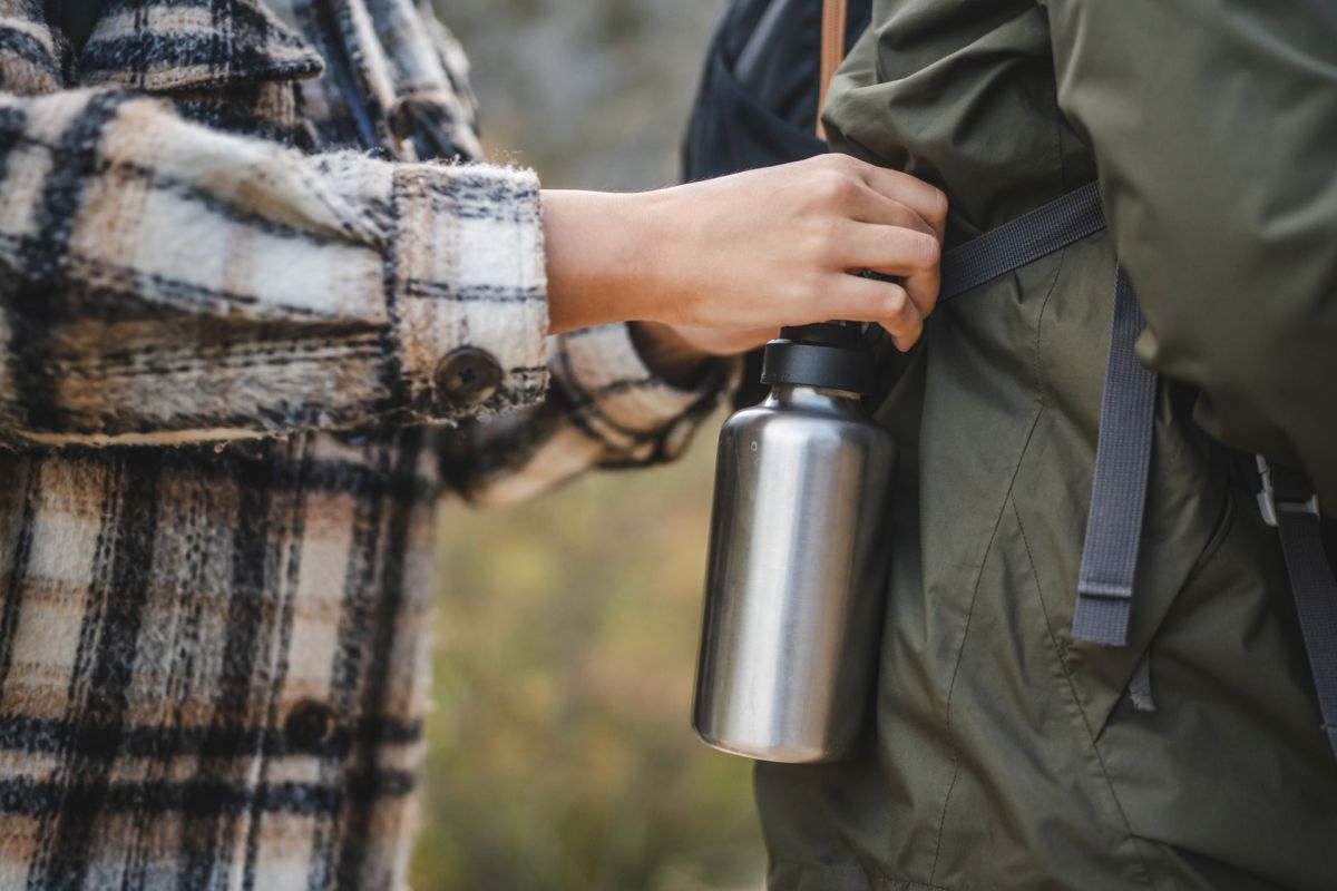 A woman attaching a metal water bottle to a backpack.