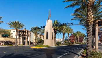 A street view of an entrance archway to a historic downtown area surrounded by palm trees.