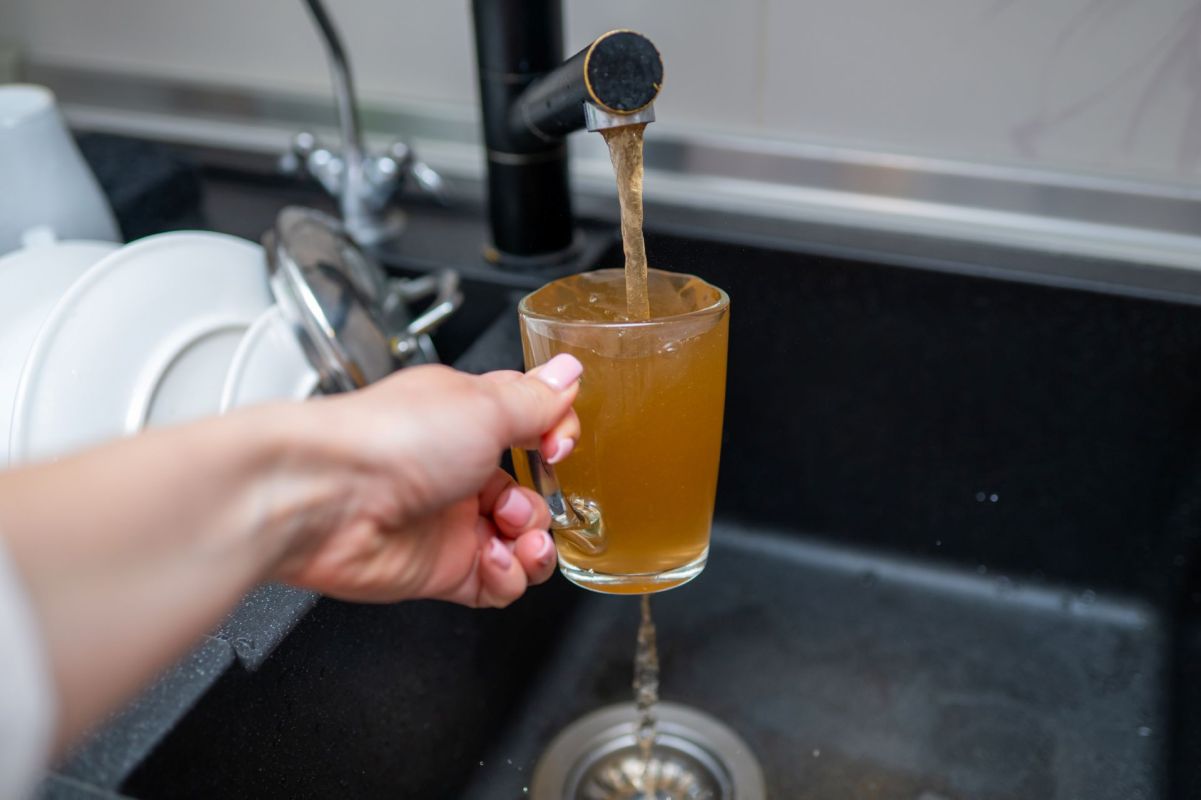 A person filling a glass with brown tap water.