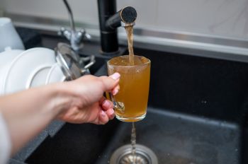 A person filling a glass with brown tap water.