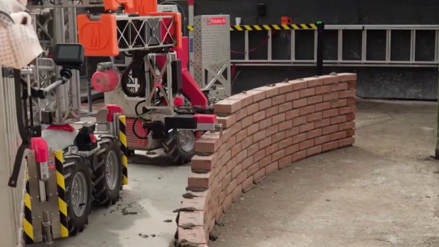 A robotic machine placing bricks in a curved pattern on a construction site.