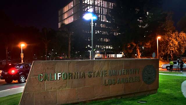 The sign for California State University, Los Angeles, is illuminated at night, with a building and streetlights in the background.