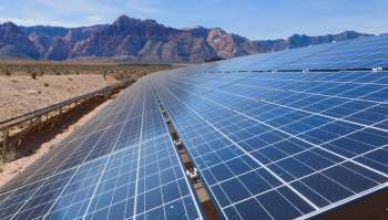 Solar panels installed in a desert landscape with mountains in the background.