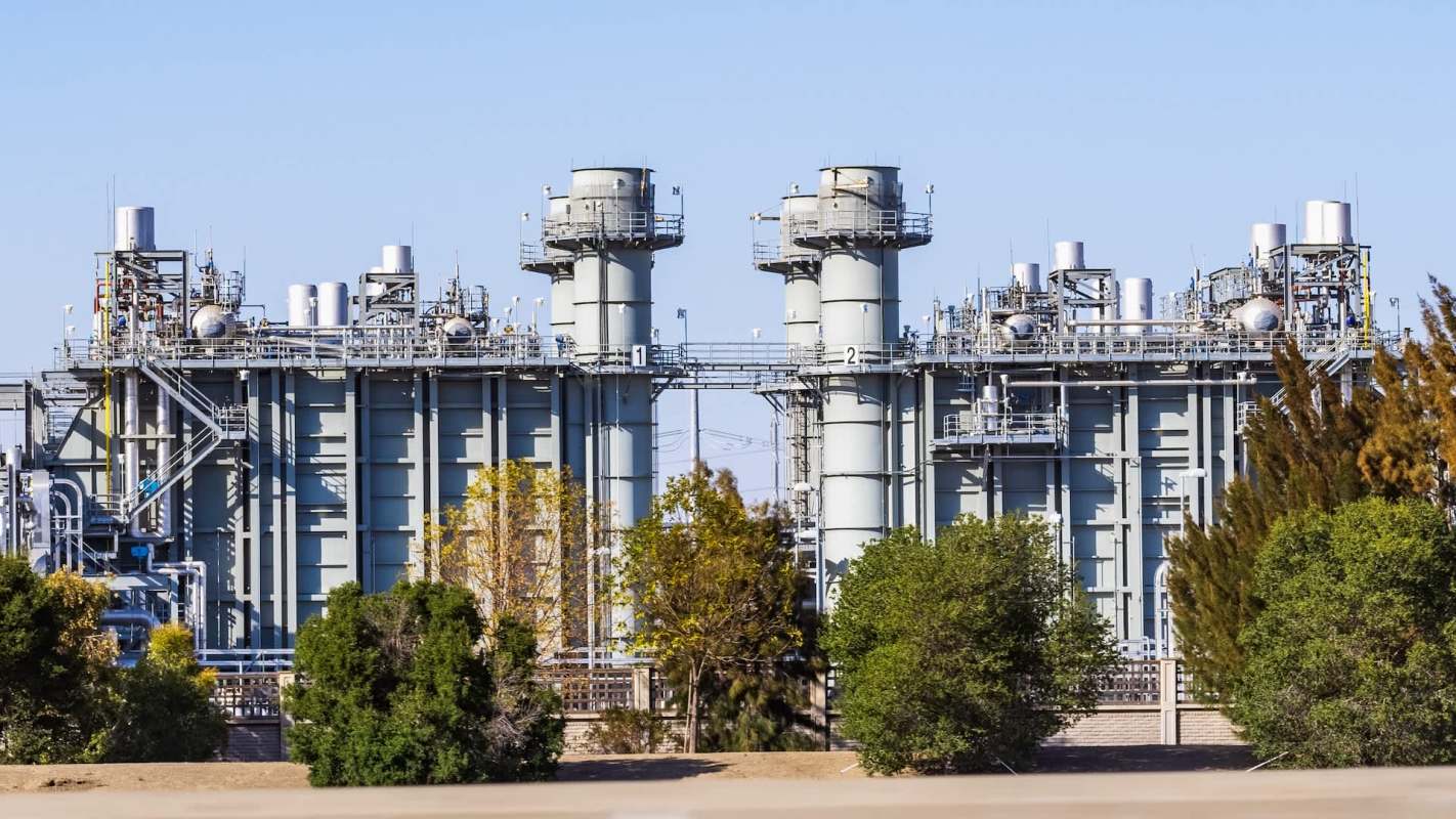 A large industrial facility with multiple towers and pipes surrounded by trees.
