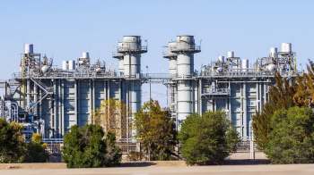 A large industrial facility with multiple towers and pipes surrounded by trees.