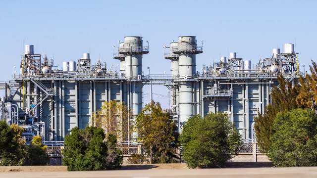 A large industrial facility with multiple towers and pipes surrounded by trees.