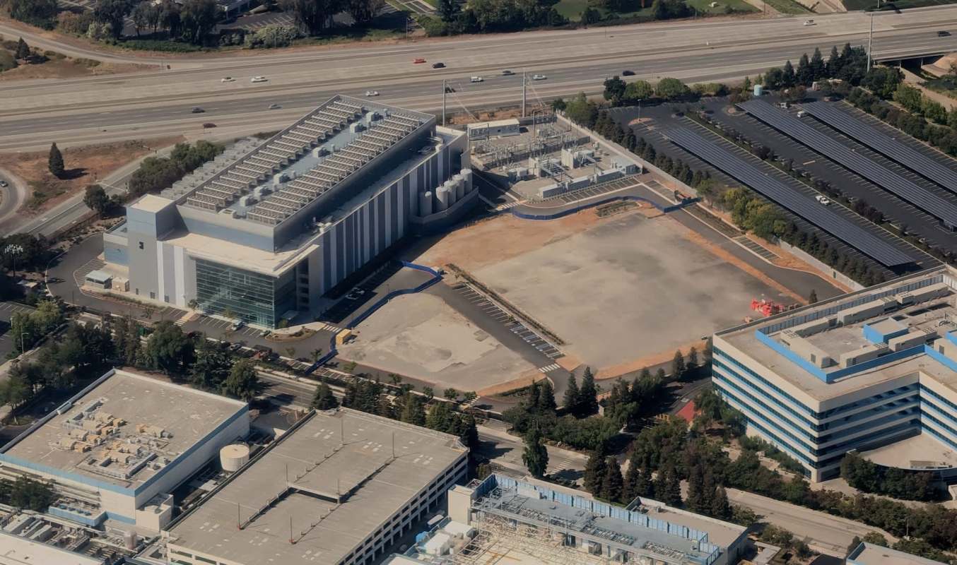 An aerial view of a commercial complex with a large data center, parking lots, and an empty lot nearby.