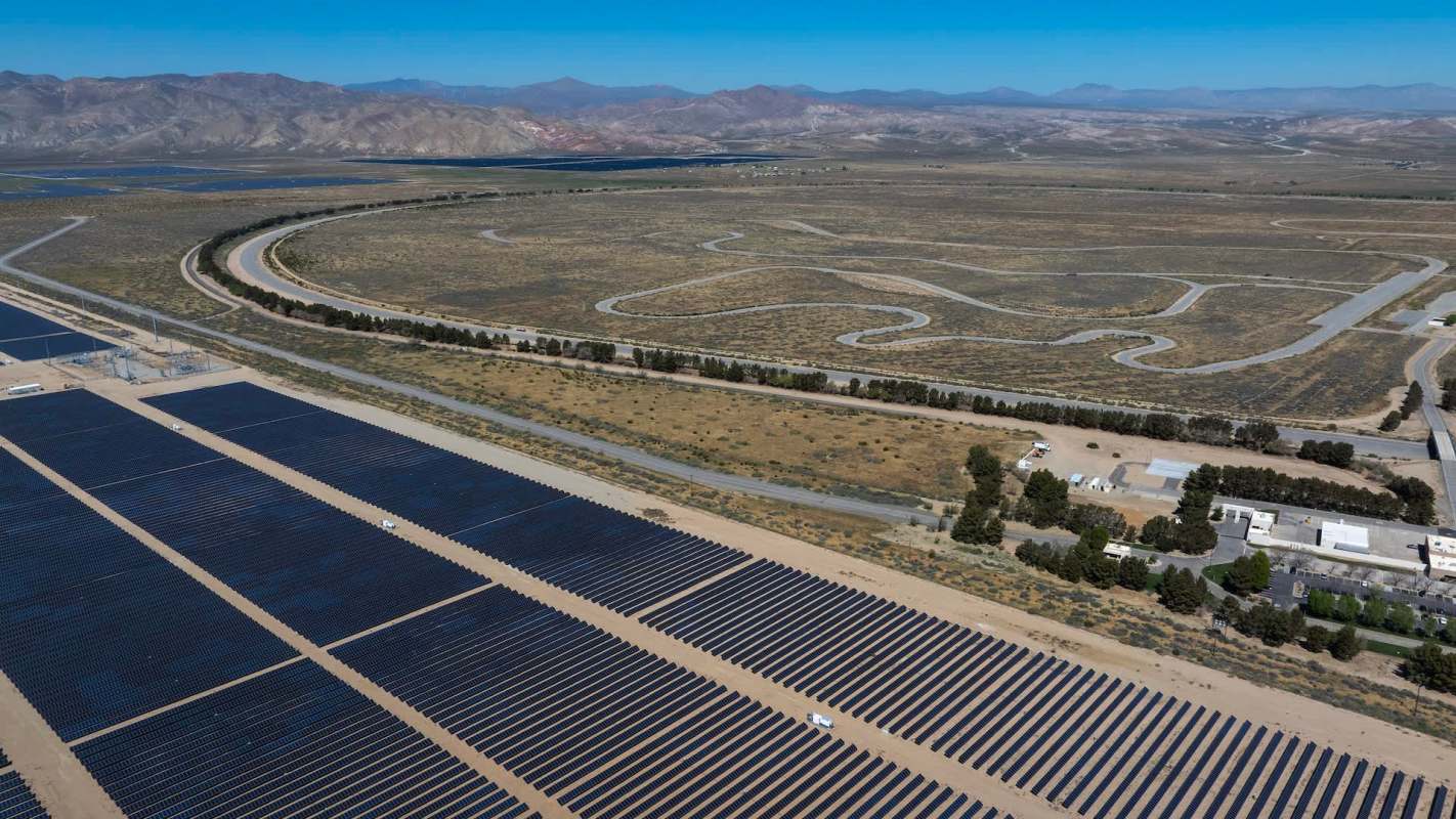 A large solar panel field with winding roads and mountains in the background.