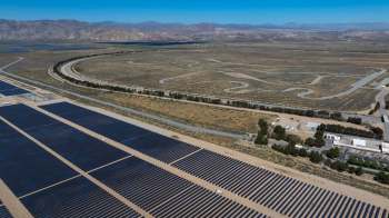 A large solar panel field with winding roads and mountains in the background.