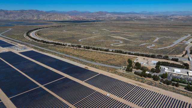 A large solar panel field with winding roads and mountains in the background.