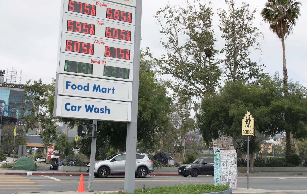 A gas station sign displaying $5.75 for regular fuel, alongside parked cars and trees.