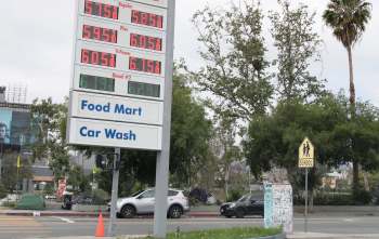 A gas station sign displaying $5.75 for regular fuel, alongside parked cars and trees.
