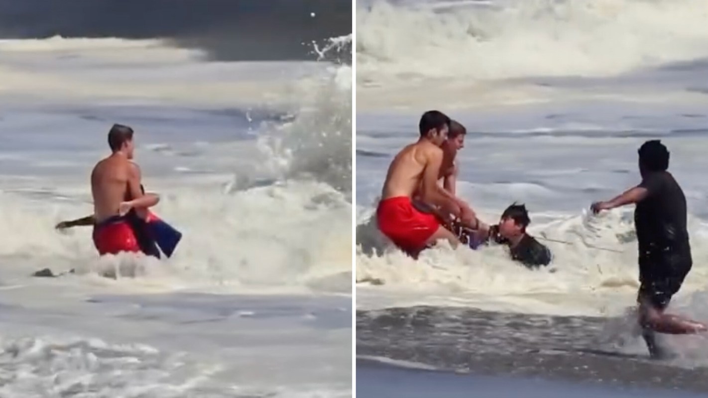 Four people assist someone in the water as waves crash around them.