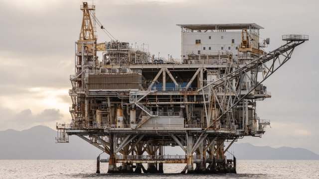 An oil drilling platform stands in the ocean with hills visible in the background.
