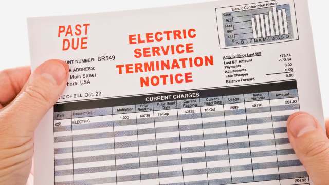 A person holds an electric service termination notice with past due payment details.