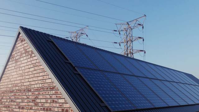 A roof with solar panels and power lines in the background under a clear blue sky.