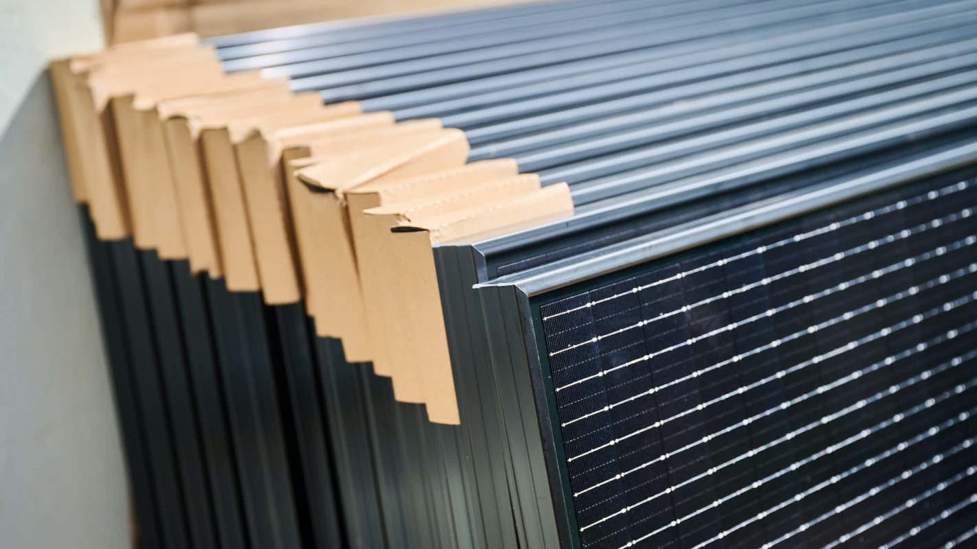 Stacks of solar panels partially covered with cardboard for protection.