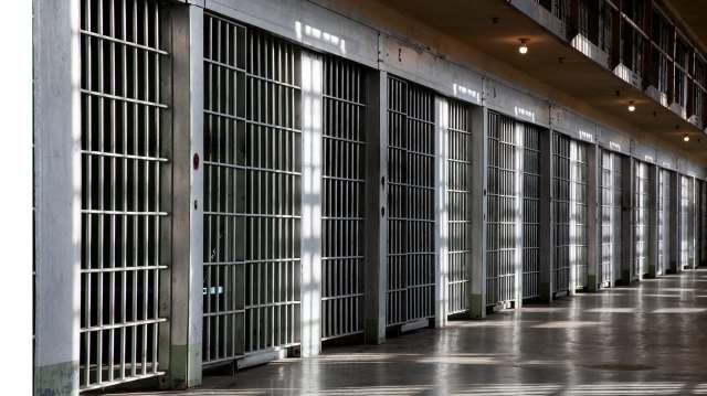 A row of prison cell doors with bars in a dimly lit corridor.