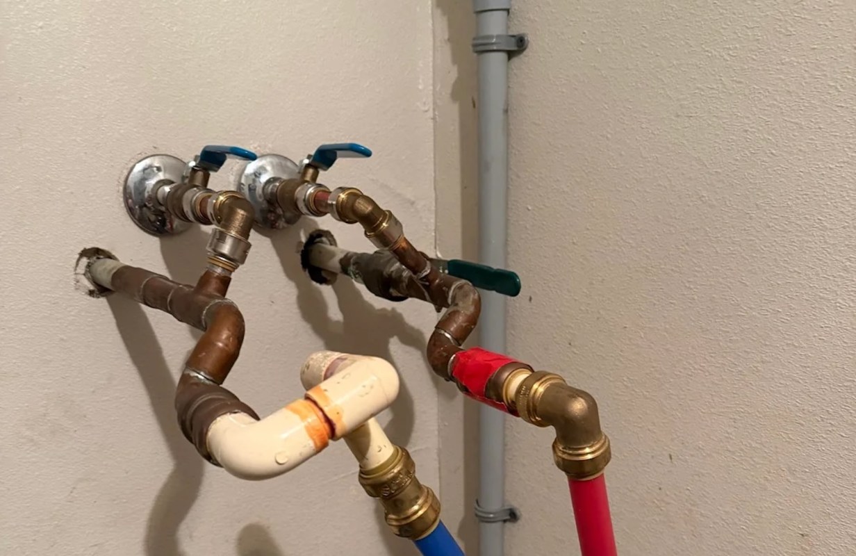 Various plumbing pipes and valves are installed on a wall, with brown, white, red, and blue components.