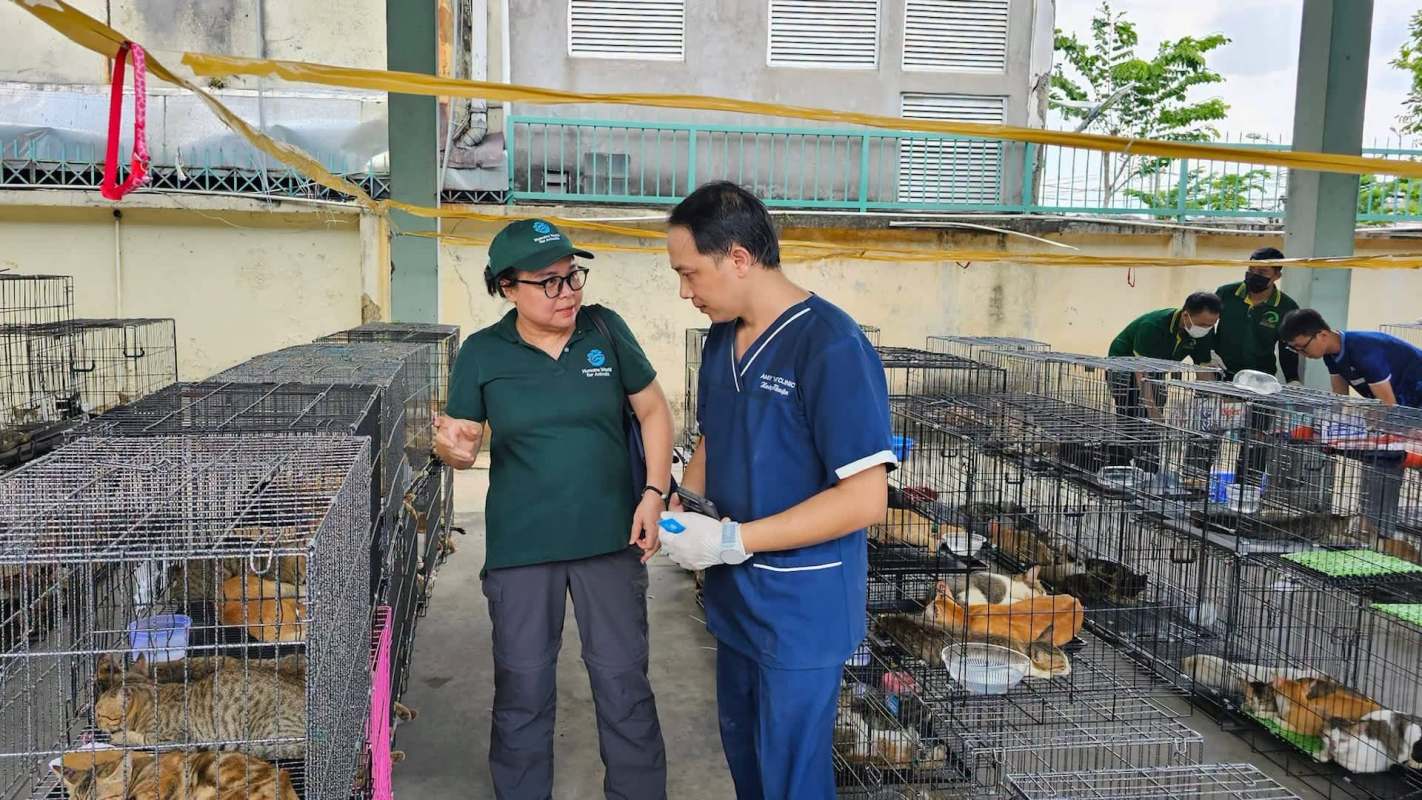 Two people discuss among cages filled with animals in a facility.