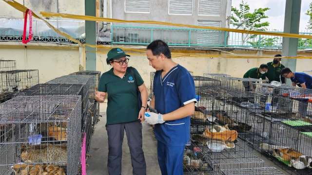 Two people discuss among cages filled with animals in a facility.