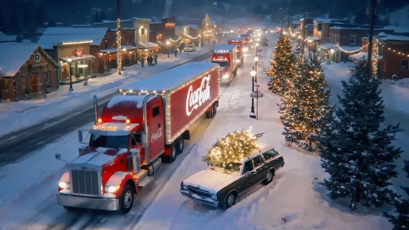 A Coca-Cola truck drives through a snowy, decorated town during the holiday season.