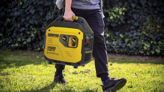 A person carrying a yellow and black portable generator on grass.