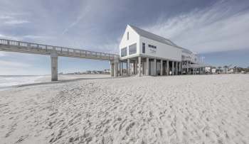 A beach with a wooden pier and a raised building on stilts overlooking the ocean.