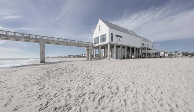 A beach with a wooden pier and a raised building on stilts overlooking the ocean.
