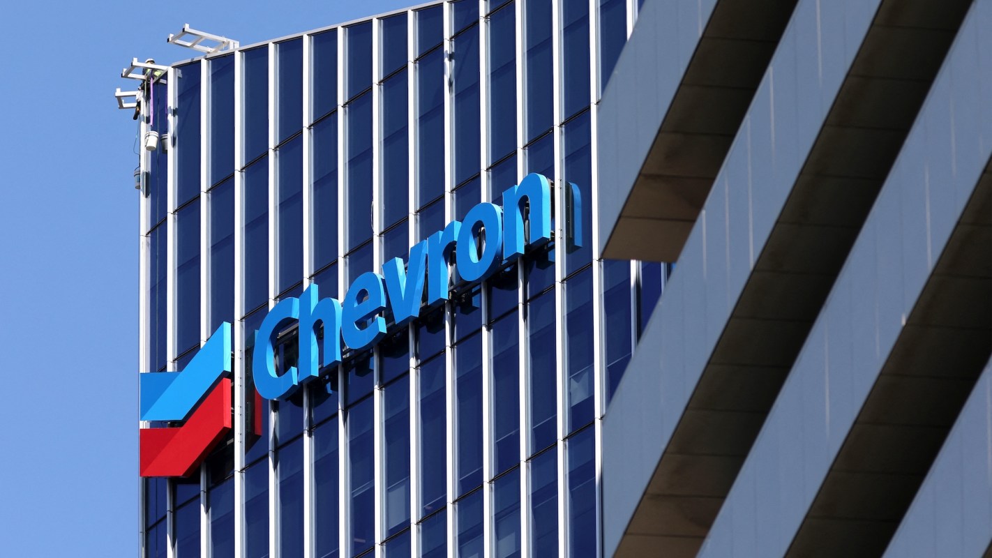 A worker performs maintenance on the exterior of a building featuring the Chevron logo.