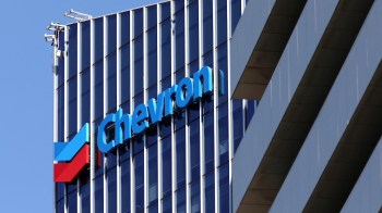 A worker performs maintenance on the exterior of a building featuring the Chevron logo.