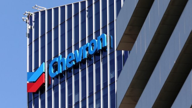 A worker performs maintenance on the exterior of a building featuring the Chevron logo.