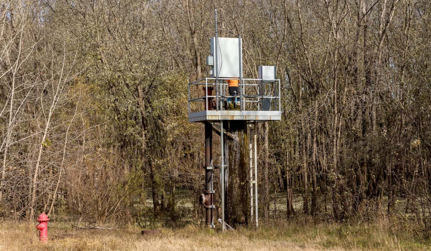 A metal platform with water pumping equipment surrounded by trees and a red fire hydrant nearby.
