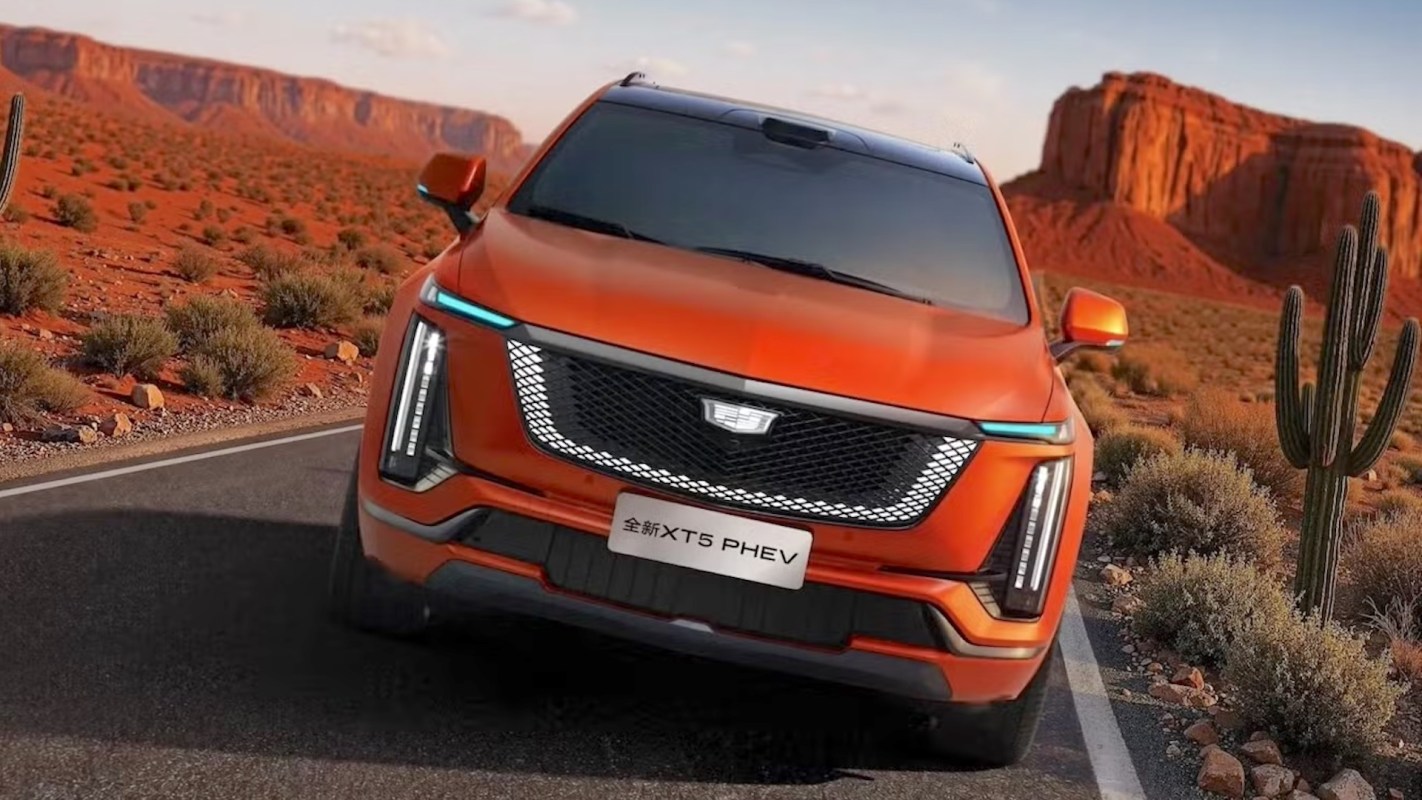 An orange Cadillac SUV on a road in a desert landscape with cacti and red rock formations.