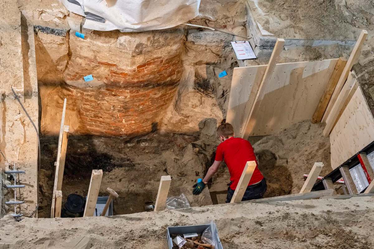 An archaeologist works in a dug site with exposed brick walls and wooden supports.