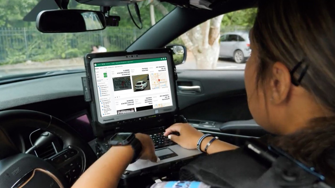 A person uses a laptop inside a vehicle displaying license plate information and maps.