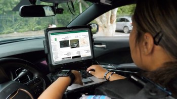A person uses a laptop inside a vehicle displaying license plate information and maps.