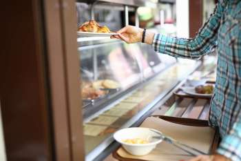 A person takes a plate of food from a display at a cafeteria.