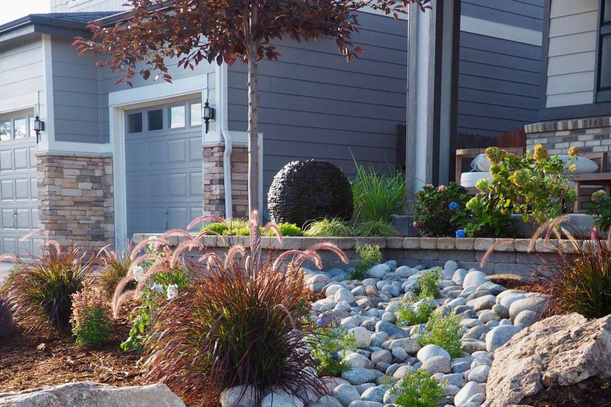 A landscaped garden with stones, grasses, and plants near a modern home.